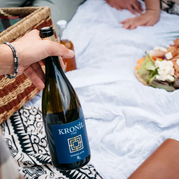 Le foto dell’Elgus Nature Retreat Mano che tiene una bottiglia di vino durante un picnic su una coperta bianca