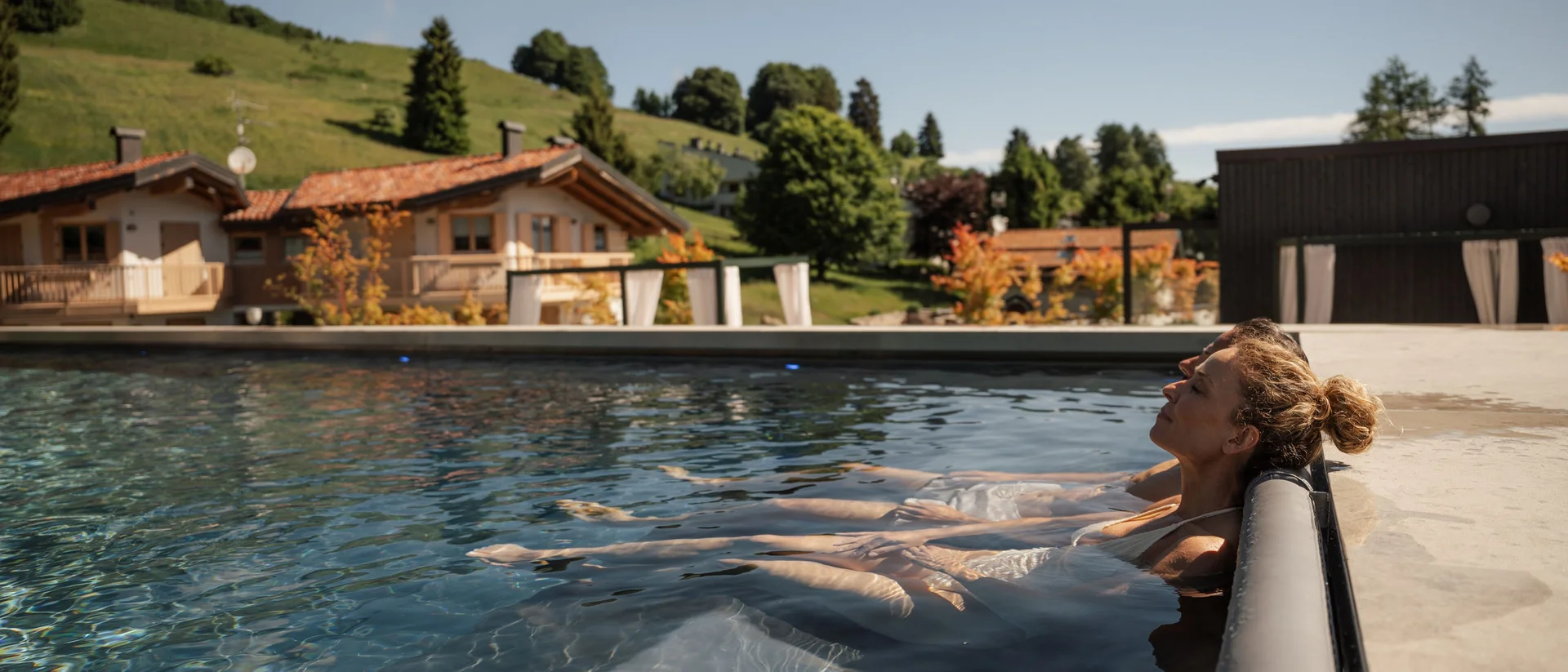 Elgus: hotel con spa adults only in Trentino Donna rilassata in piscina all'aperto con case e colline sullo sfondo