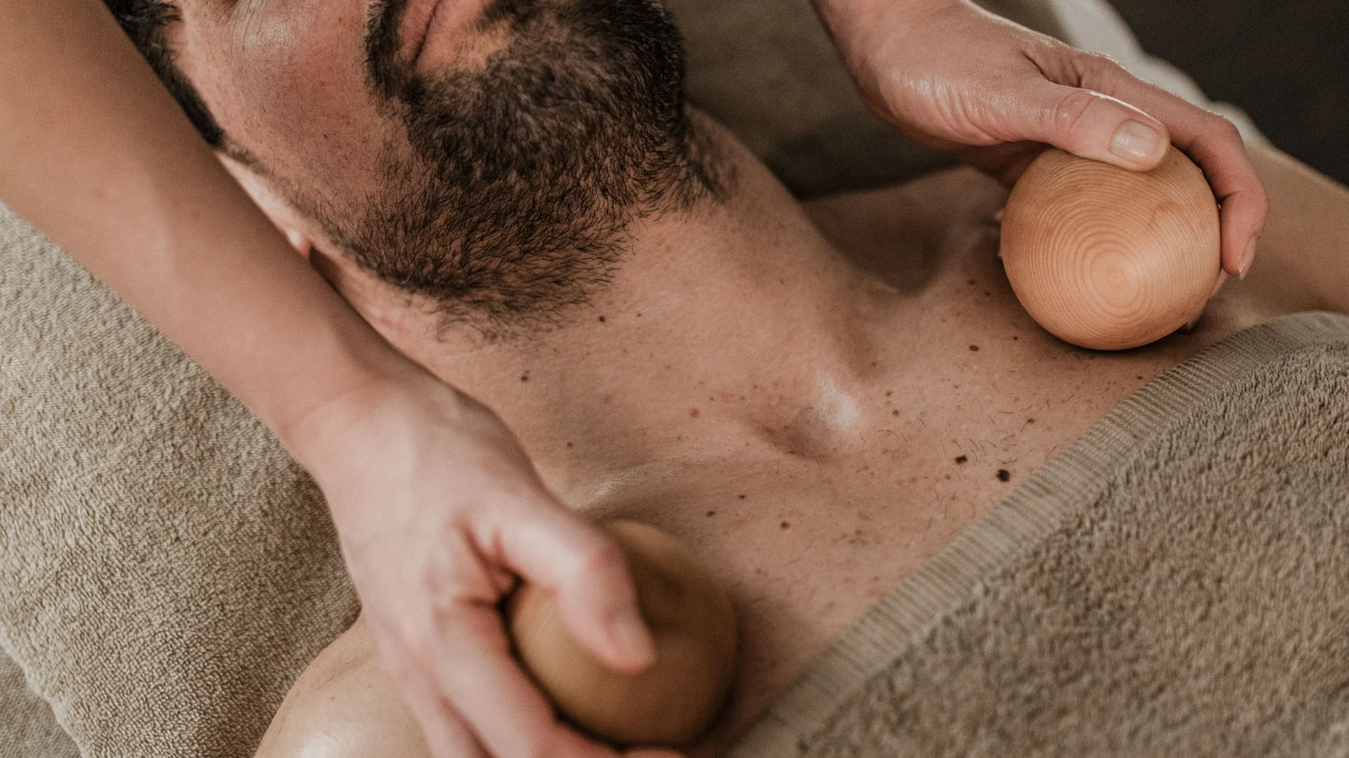 Trattamenti e massaggi in Trentino Uomo con barba che riceve massaggio al petto con strumenti di legno