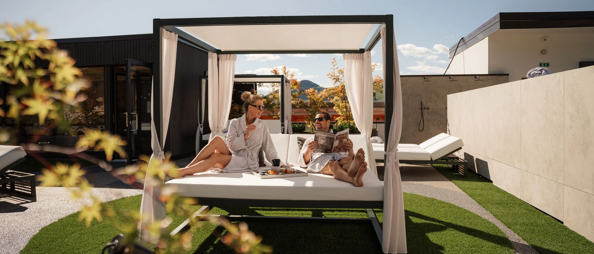 Elgus: hotel con spa adults only in Trentino Coppia rilassata su un letto da esterno con tenda in un giardino soleggiato