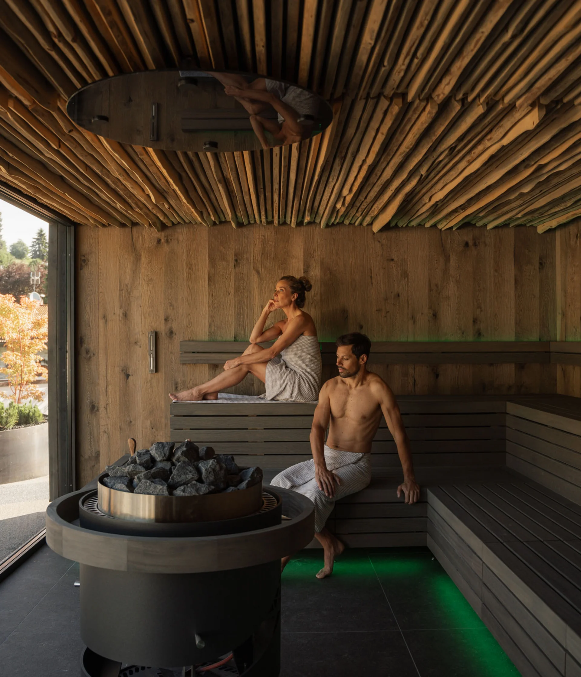 Elgus: hotel con spa a Brentonico Due persone rilassate in una sauna moderna con pareti in legno e grande finestra
