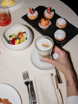Colazione con caffè latte, frutta fresca e dolcetti su tovaglia bianca