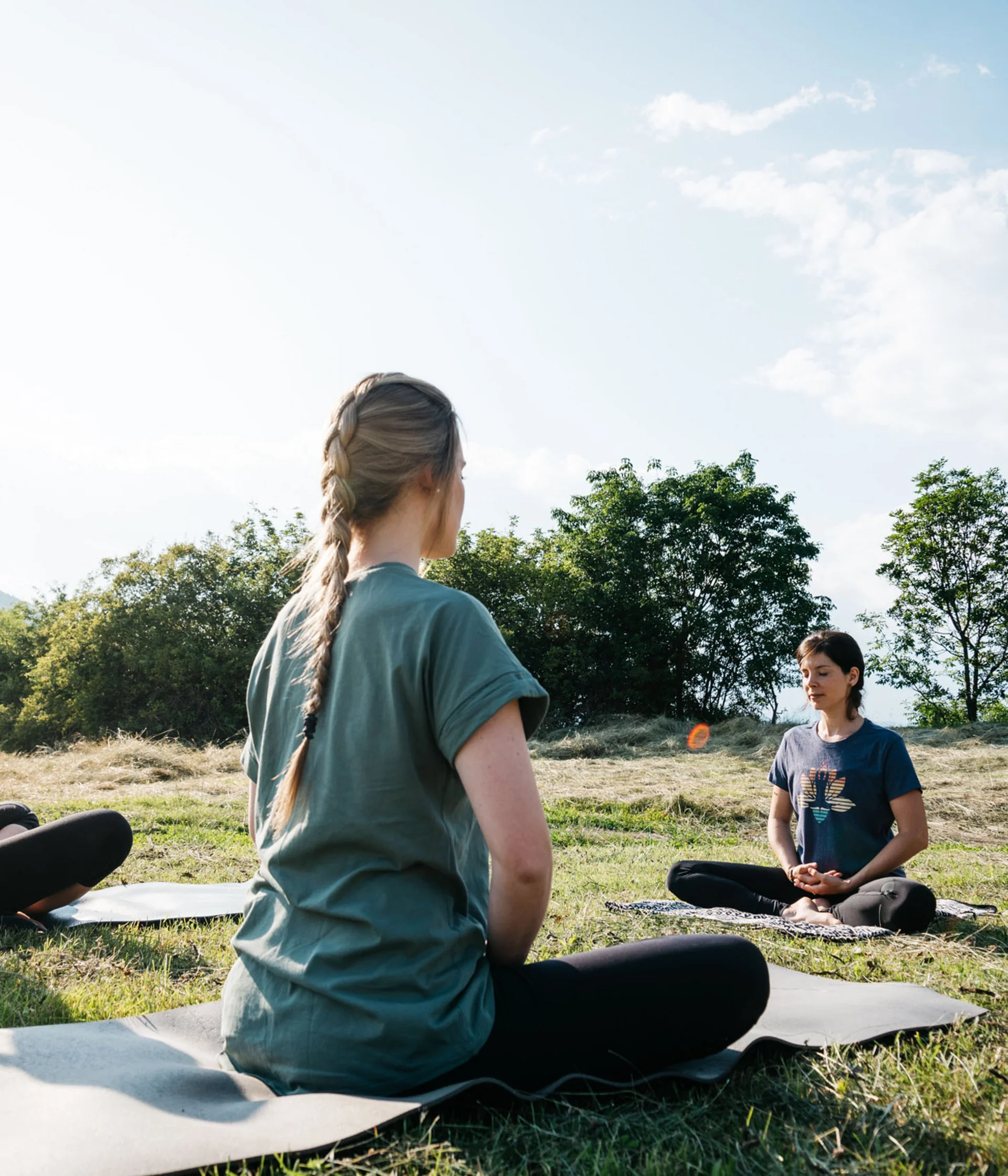 Tre donne sedute su tappetini da yoga all'aperto in un prato verde