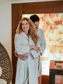 Coppia in accappatoi abbracciata in una spa con parete di sale illuminata
