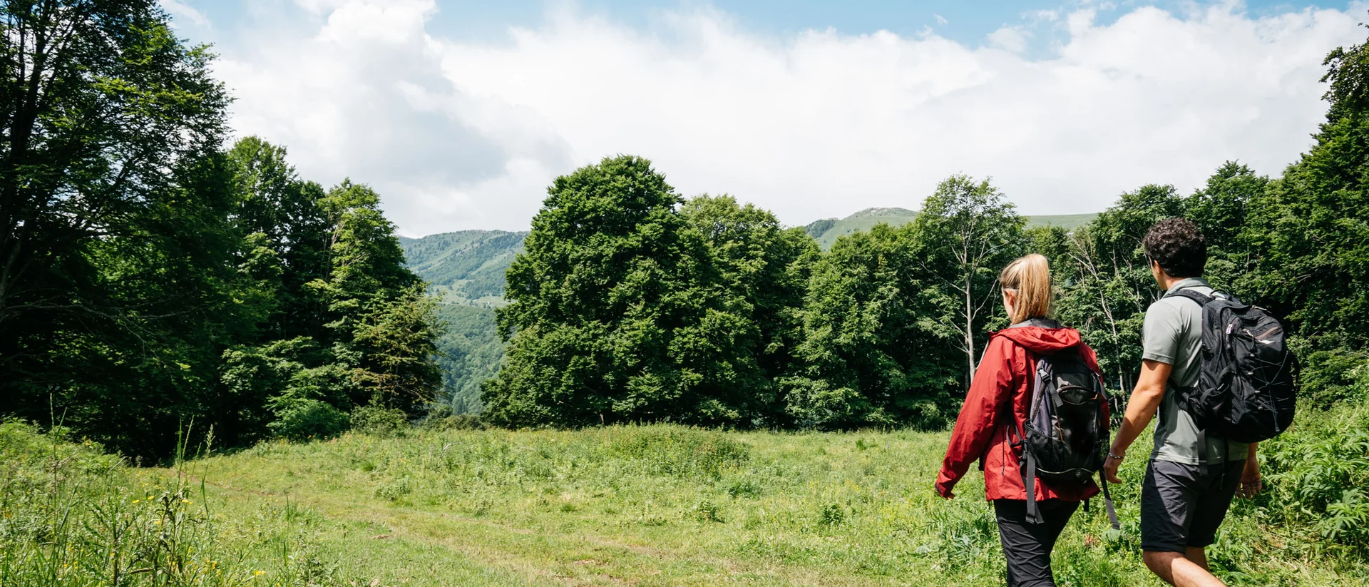 Tutto il divertimento di un hotel sul Monte Baldo Due escursionisti con zaini che camminano in un prato verde verso la foresta