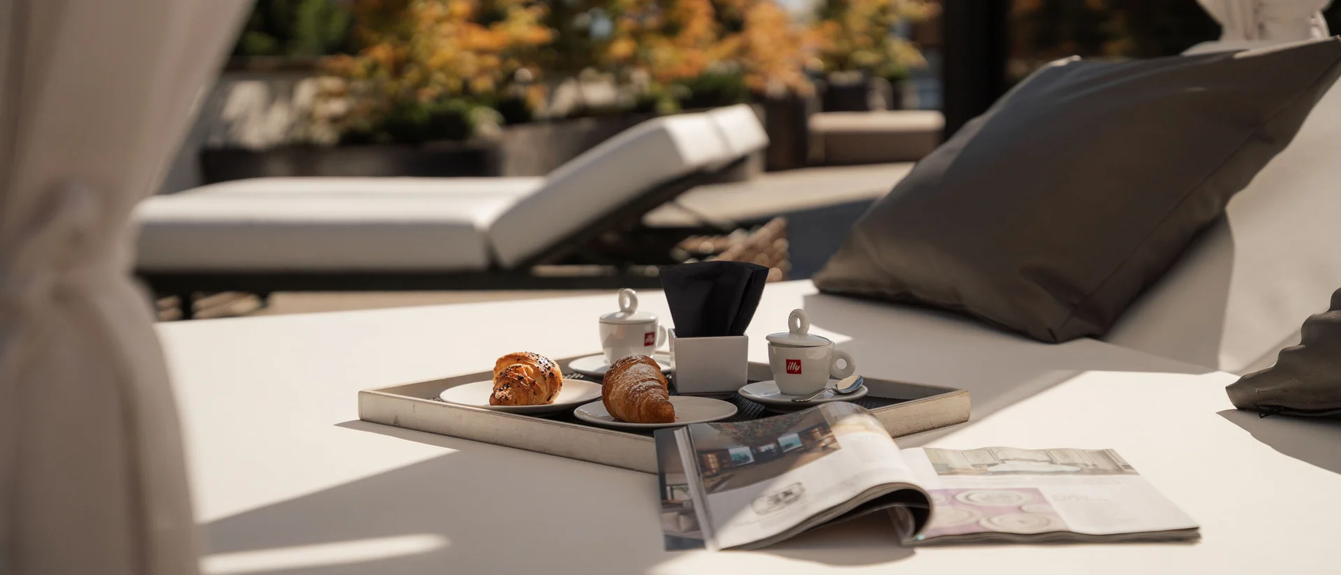 Il Forest Rooftop dell’Elgus Colazione con caffè e cornetti su lettino all'aperto con cuscini grigi
