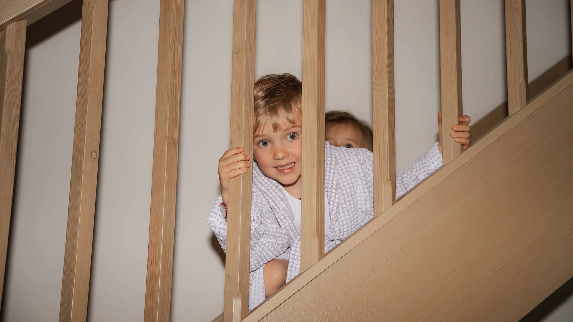 Elgus: hotel a 4 stelle in Trentino Due bambini sorridenti che guardano attraverso le sbarre di una scala in legno