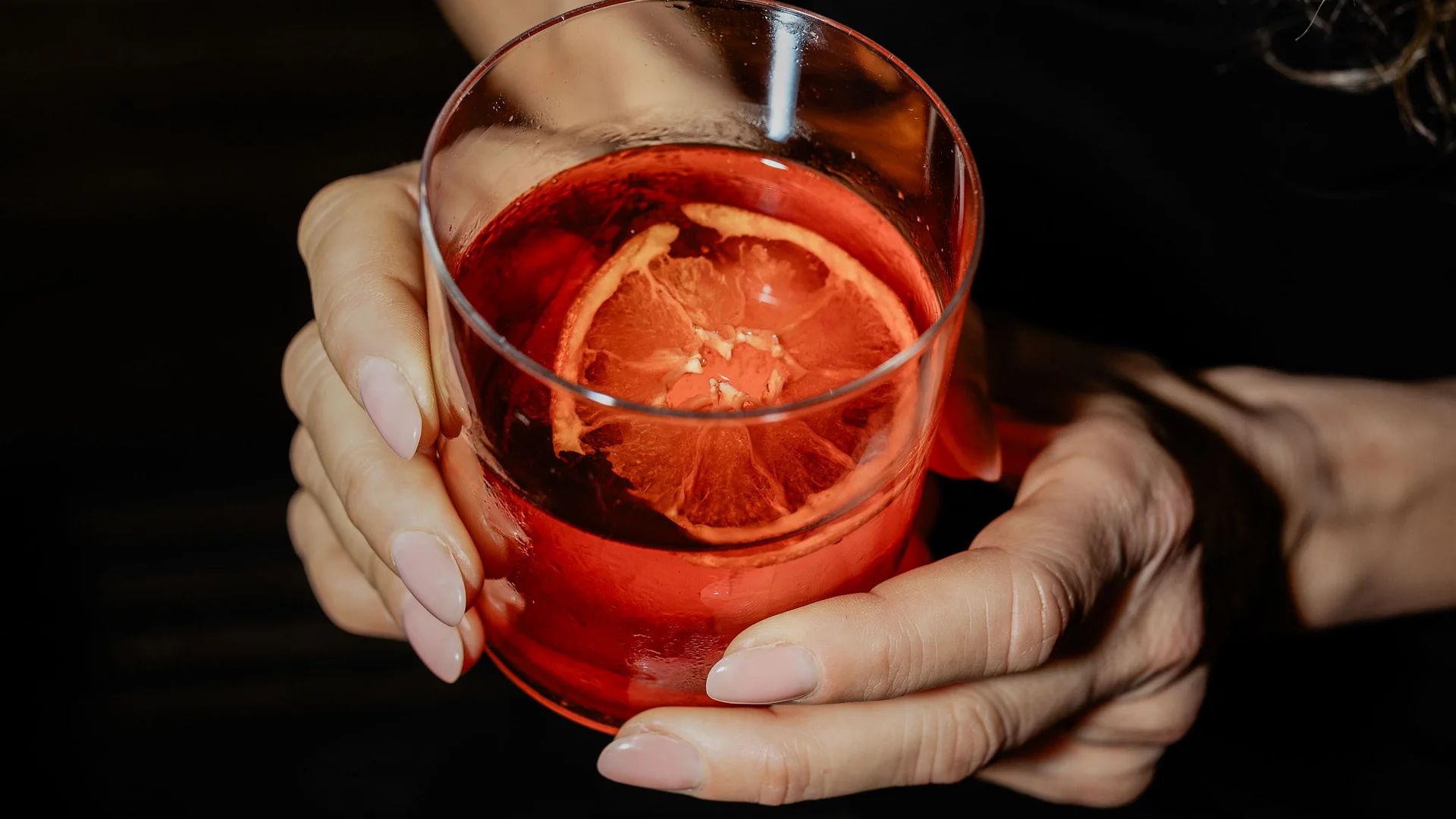Donna che tiene un bicchiere con cocktail rosso e fetta di agrume