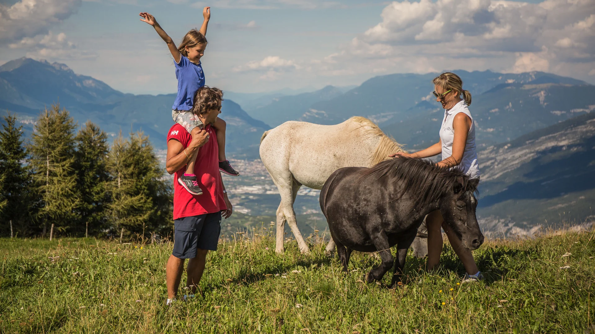 Elgus: hotel a 4 stelle in Trentino Famiglia con due cavalli su prato verde con montagne sullo sfondo