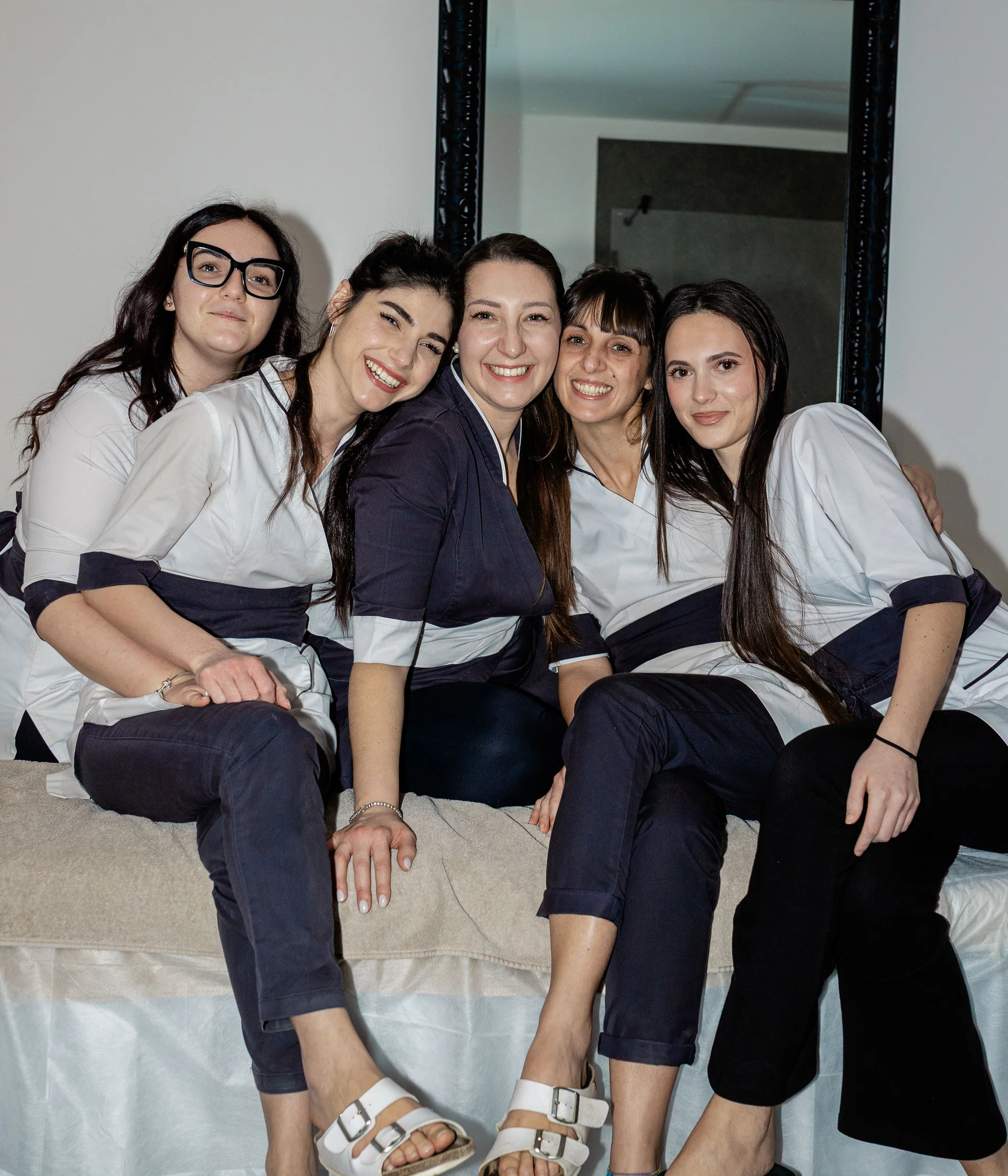 Elgus: hotel con spa a Brentonico Cinque donne sorridenti in divise da lavoro sedute insieme su un letto