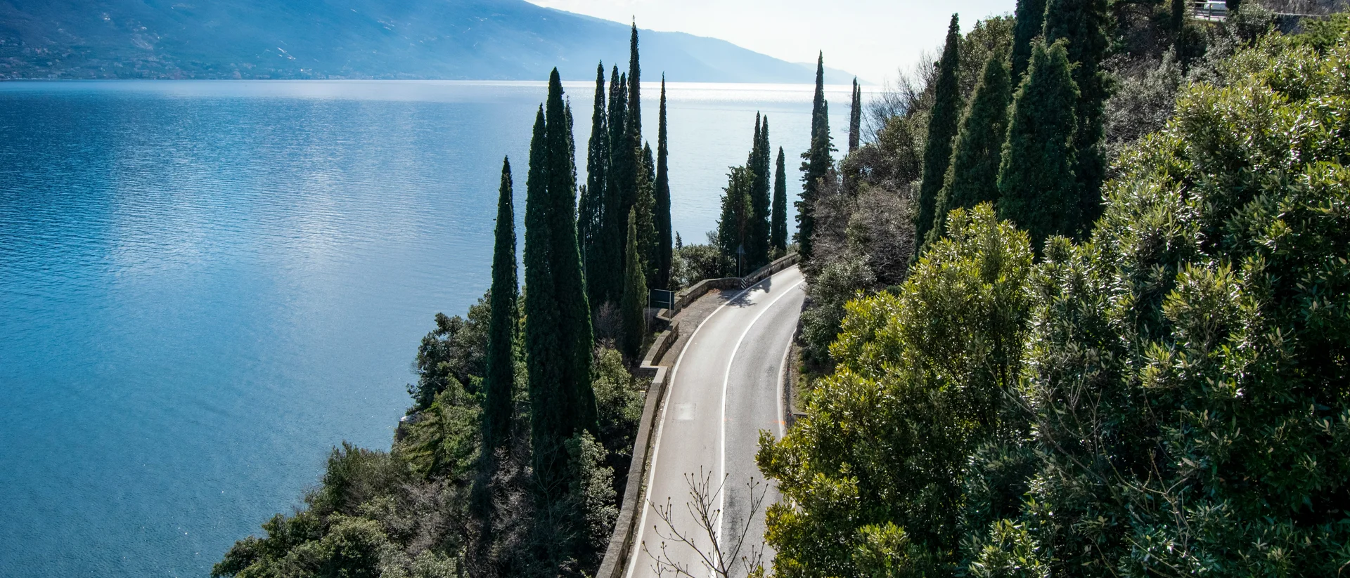 Strada panoramica con cipressi lungo un lago e montagne sullo sfondo