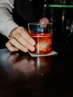 Mano che prende un bicchiere con un drink rosso e ghiaccio al bar