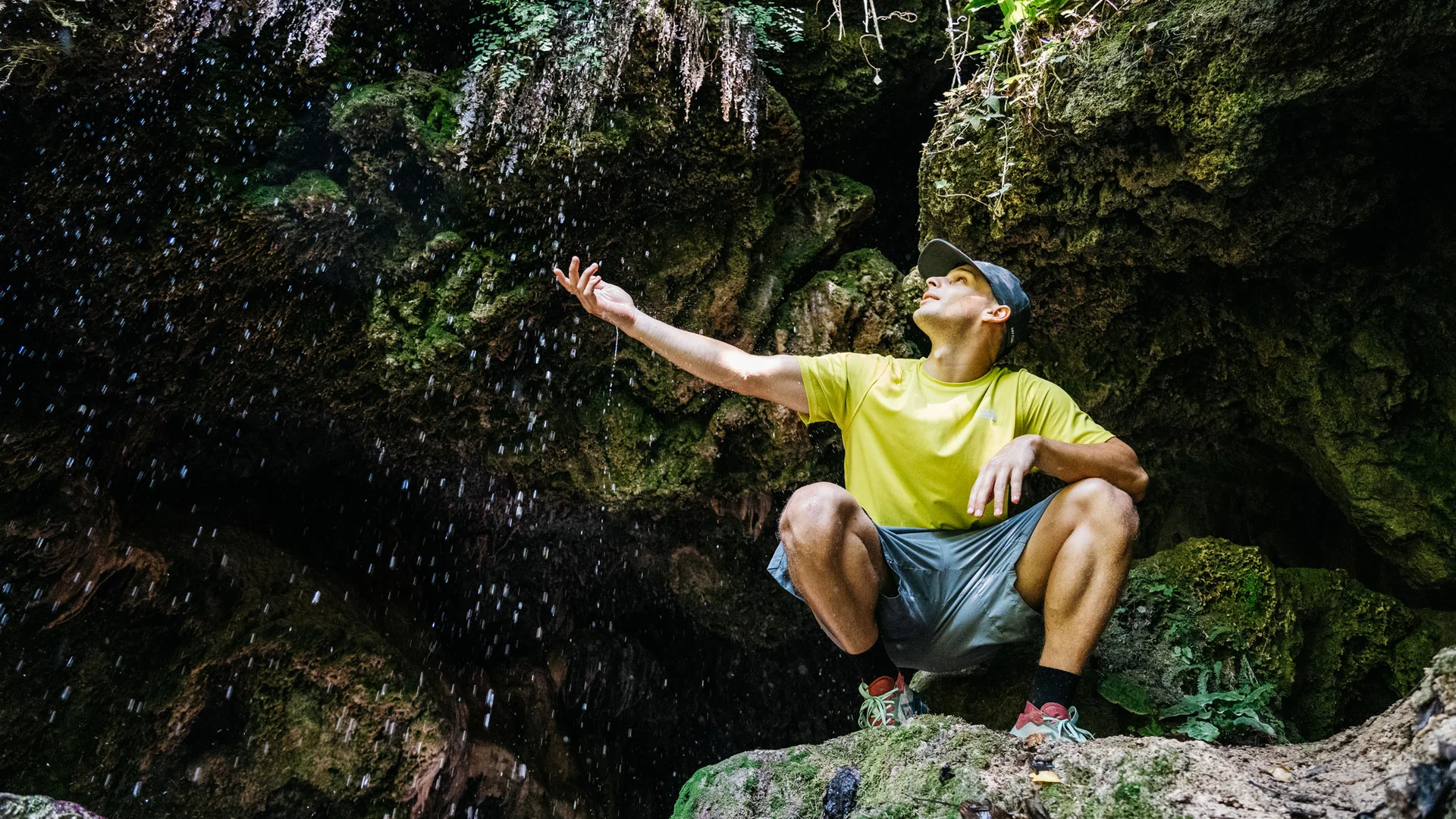 Hotel per single in Trentino Uomo in abbigliamento sportivo accovacciato vicino a una cascata in grotta verde