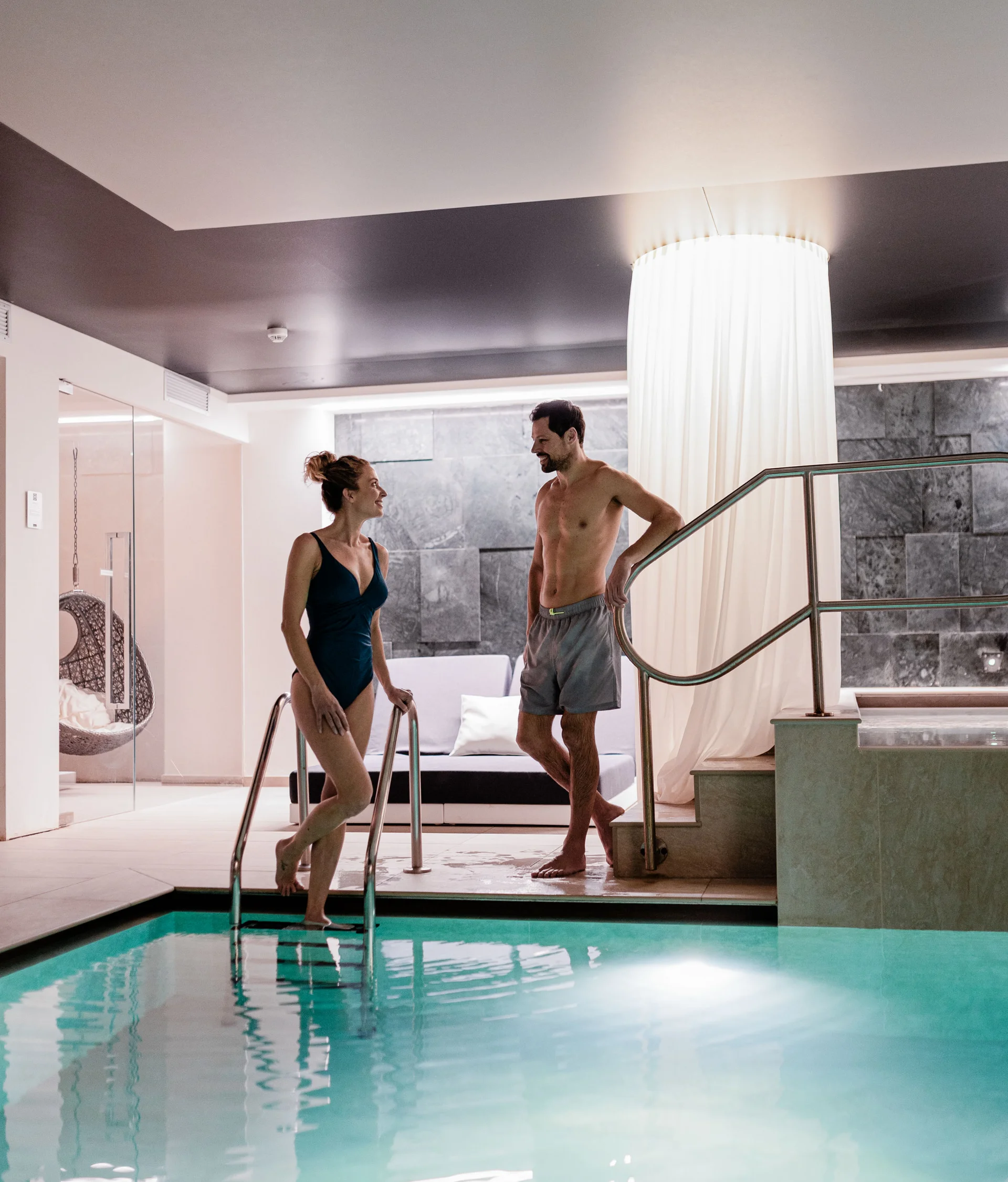 Day spa in Trentino, all’Elgus Coppia che parla vicino a una piscina interna in un ambiente moderno e rilassante