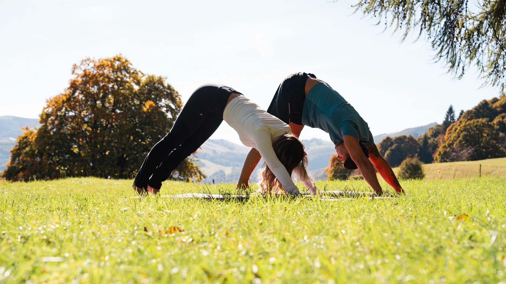 Elgus: hotel a 4 stelle in Trentino Due persone fanno yoga all'aperto su un prato verde in campagna