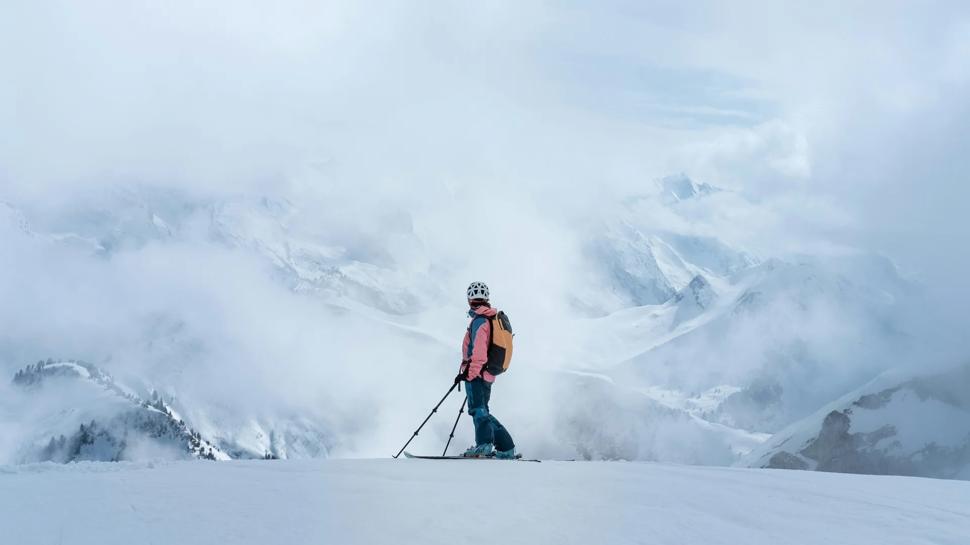 Sciatore con casco e zaino sulla neve con montagne nebbiose sullo sfondo