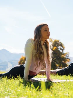 Donna che fa stretching all'aperto su un prato verde con alberi e montagne sullo sfondo