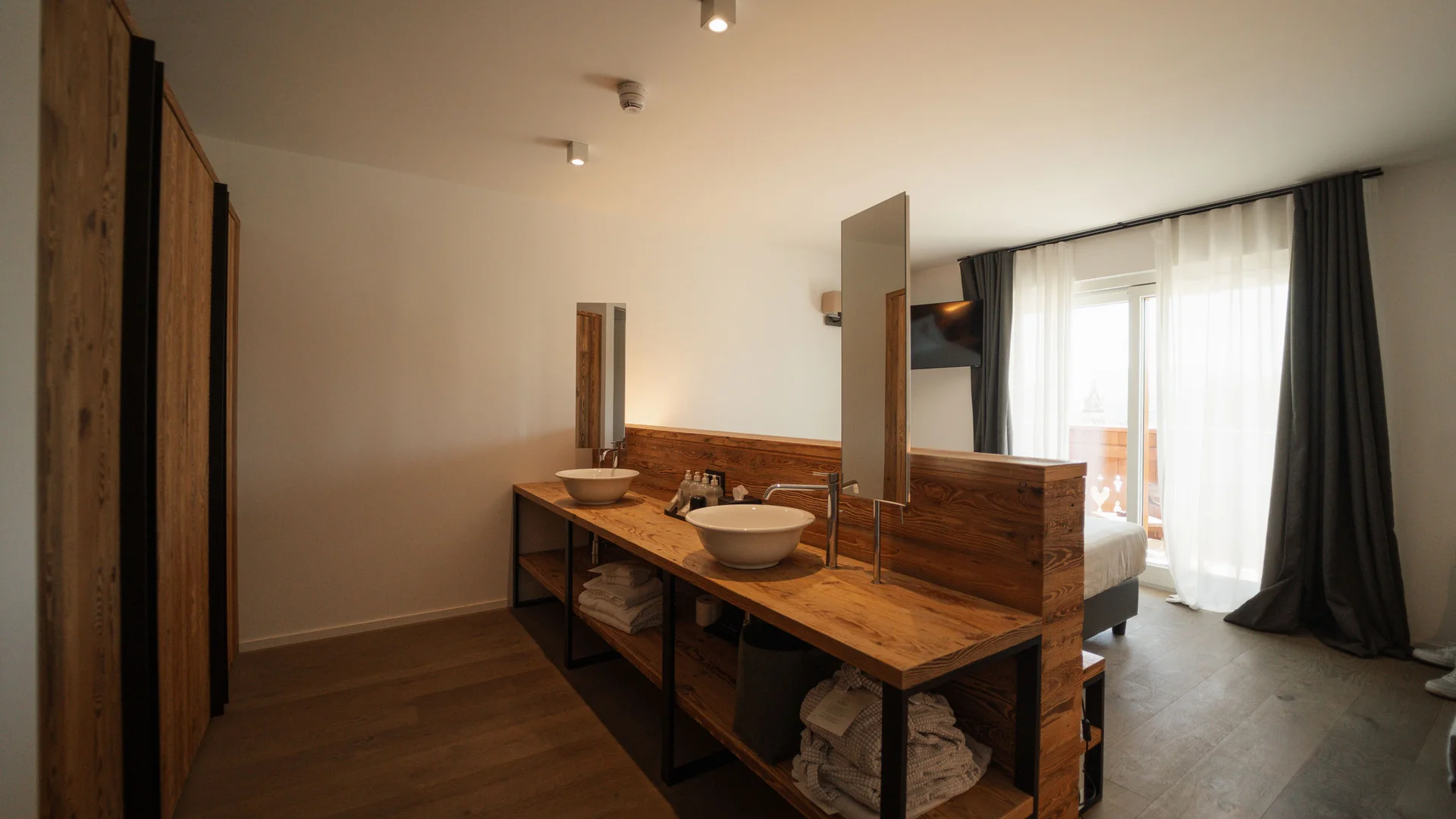 Elgus: hotel a 4 stelle in Trentino Camera d'albergo con lavabo doppio, specchio e balcone con tende bianche