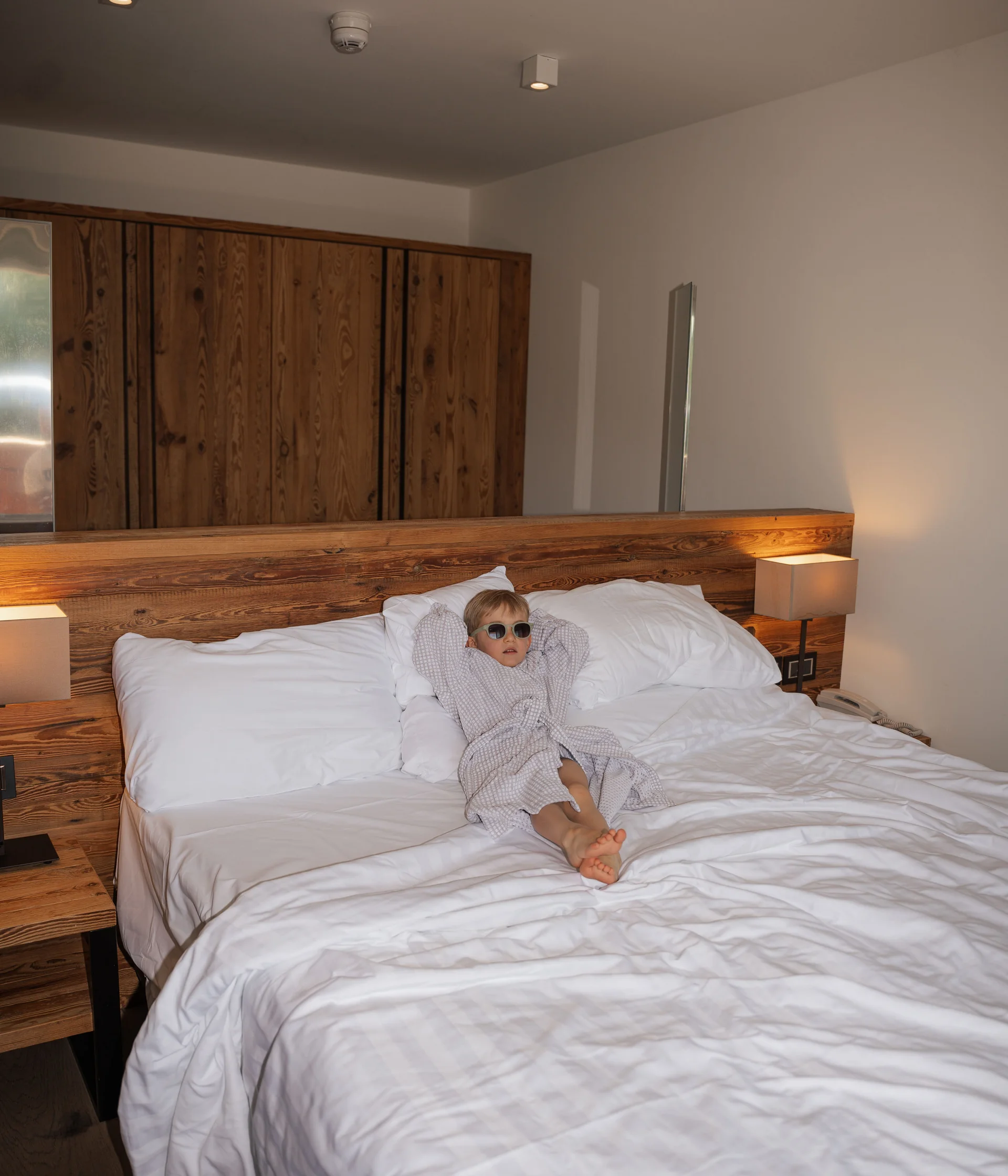 Elgus: family hotel a Brentonico Bambino con occhiali da sole e accappatoio sdraiato su letto grande in camera d'albergo