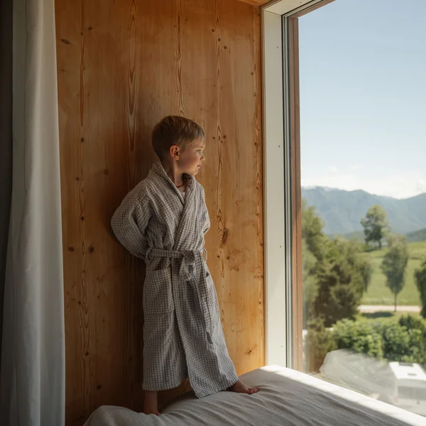Le foto dell’Elgus Nature Retreat Bambino in accappatoio che guarda fuori dalla finestra in una stanza di legno