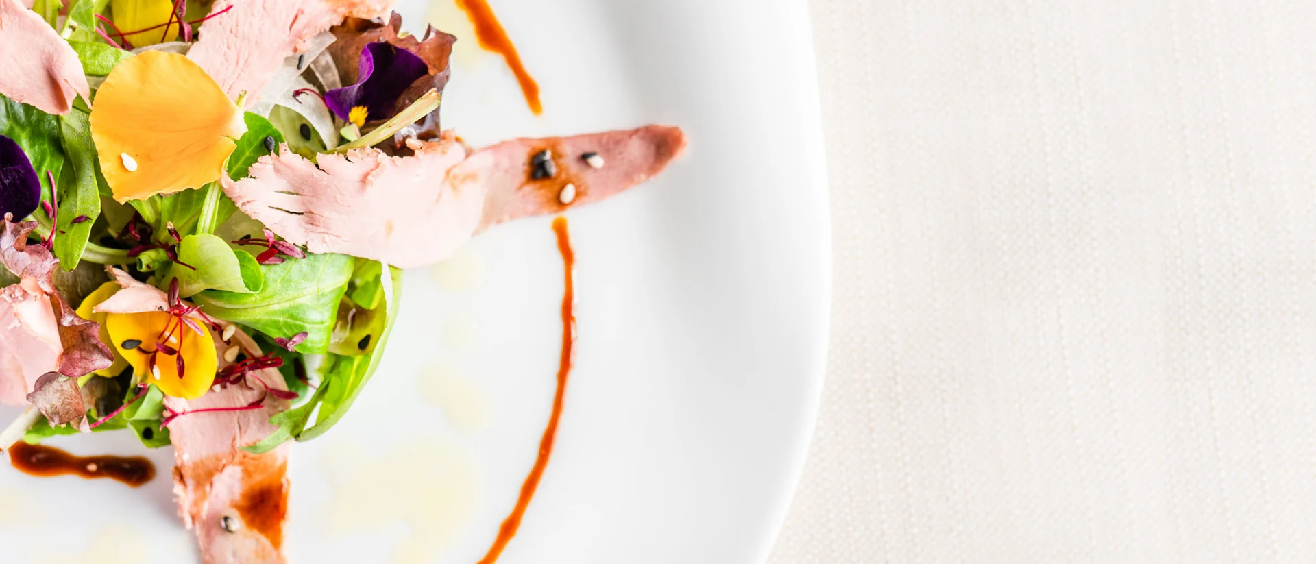 Il nostro ristorante a San Giacomo, Brentonico Insalata gourmet con fette di carne e petali di fiori su piatto bianco