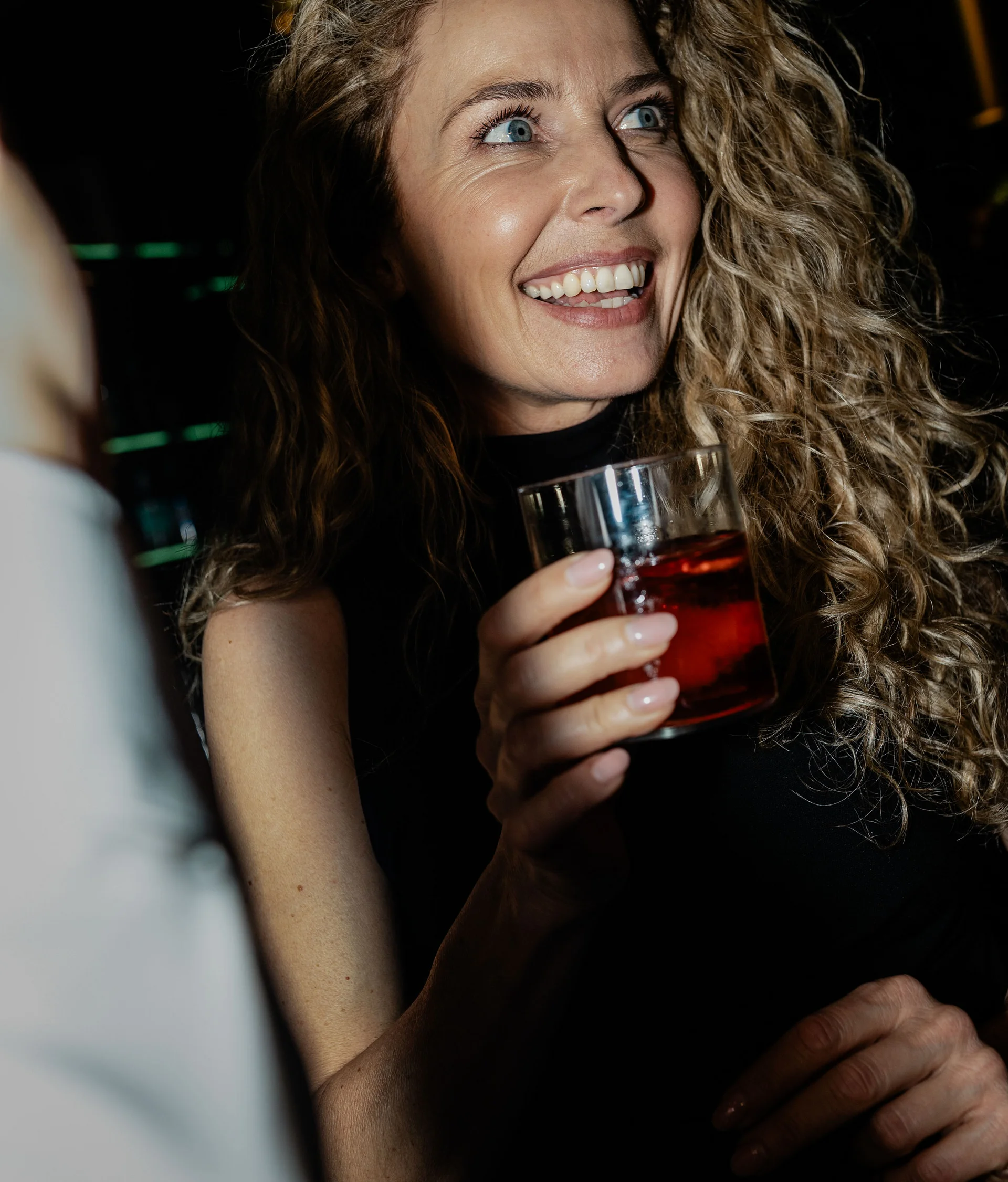 Lounge bar e bistrot a San Giacomo Donna sorridente con capelli ricci che tiene un bicchiere con bevanda rossa