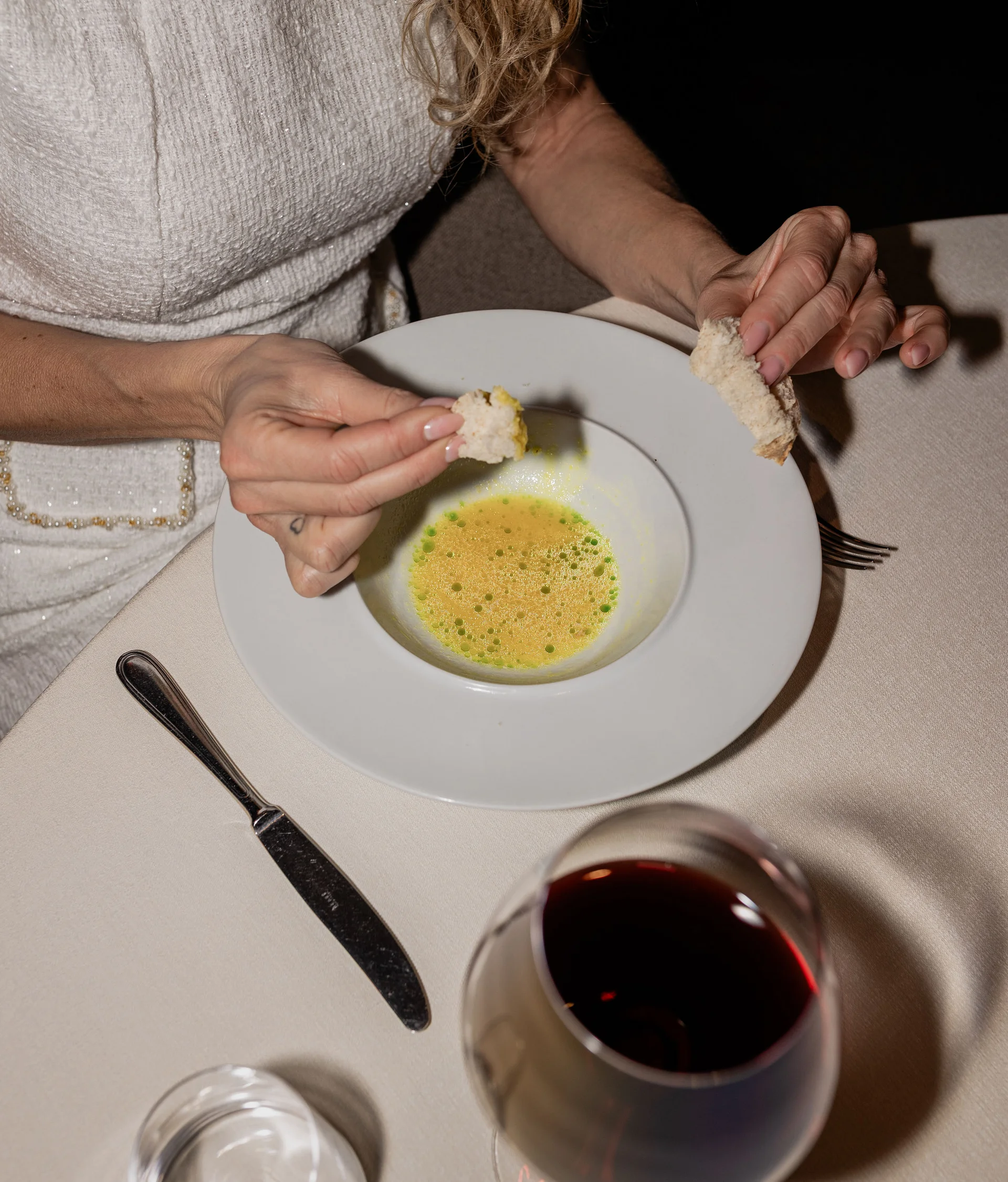 Il nostro ristorante a San Giacomo, Brentonico Donna che intinge pane in una zuppa gialla con gocce verdi in un piatto bianco