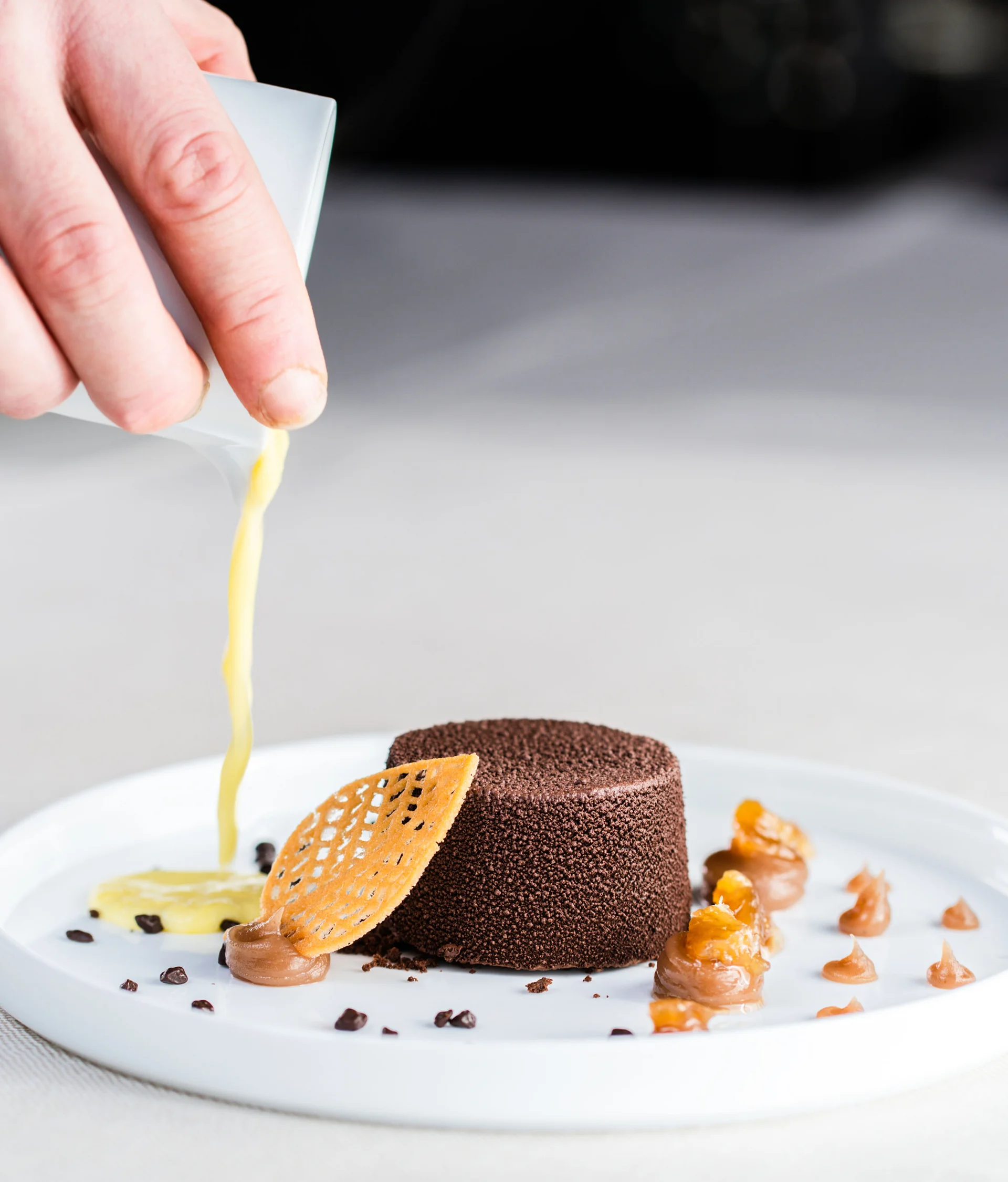 Il nostro ristorante a San Giacomo, Brentonico mano che versa salsa su dolce al cioccolato con decorazioni su piatto bianco