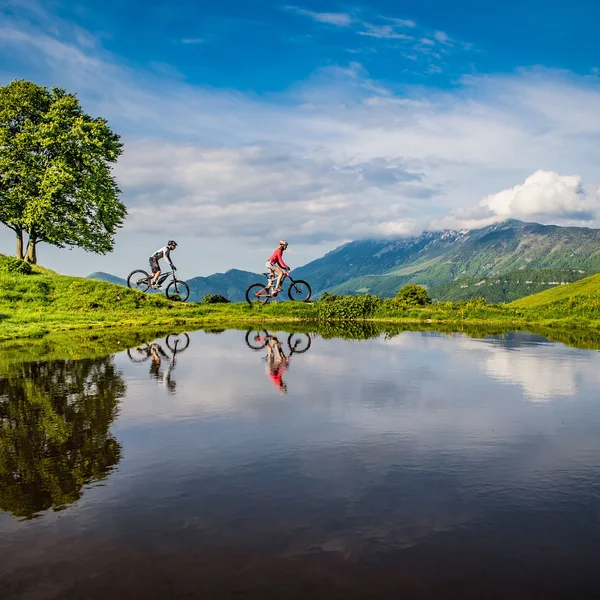 Le foto dell’Elgus Nature Retreat Due ciclisti su sentiero verde vicino a lago con riflesso di albero e montagne