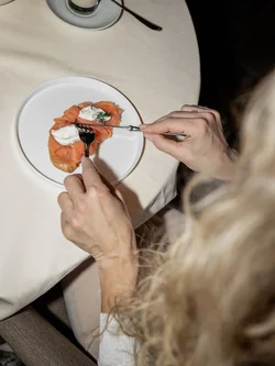 Persona che mangia pane con salmone affumicato e crema su un piatto bianco