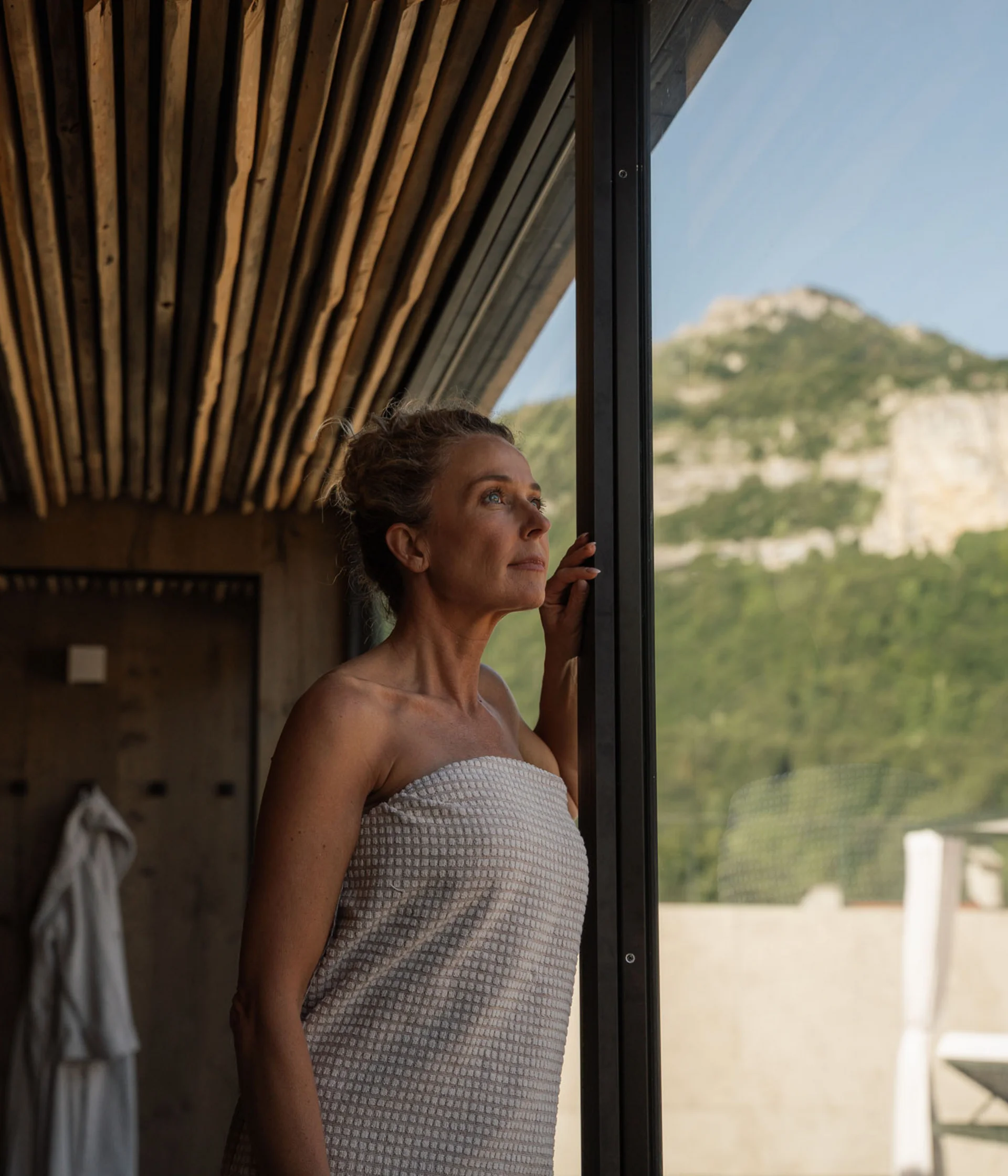 Hotel per single in Trentino Donna avvolta in asciugamano che guarda fuori dalla finestra verso le montagne