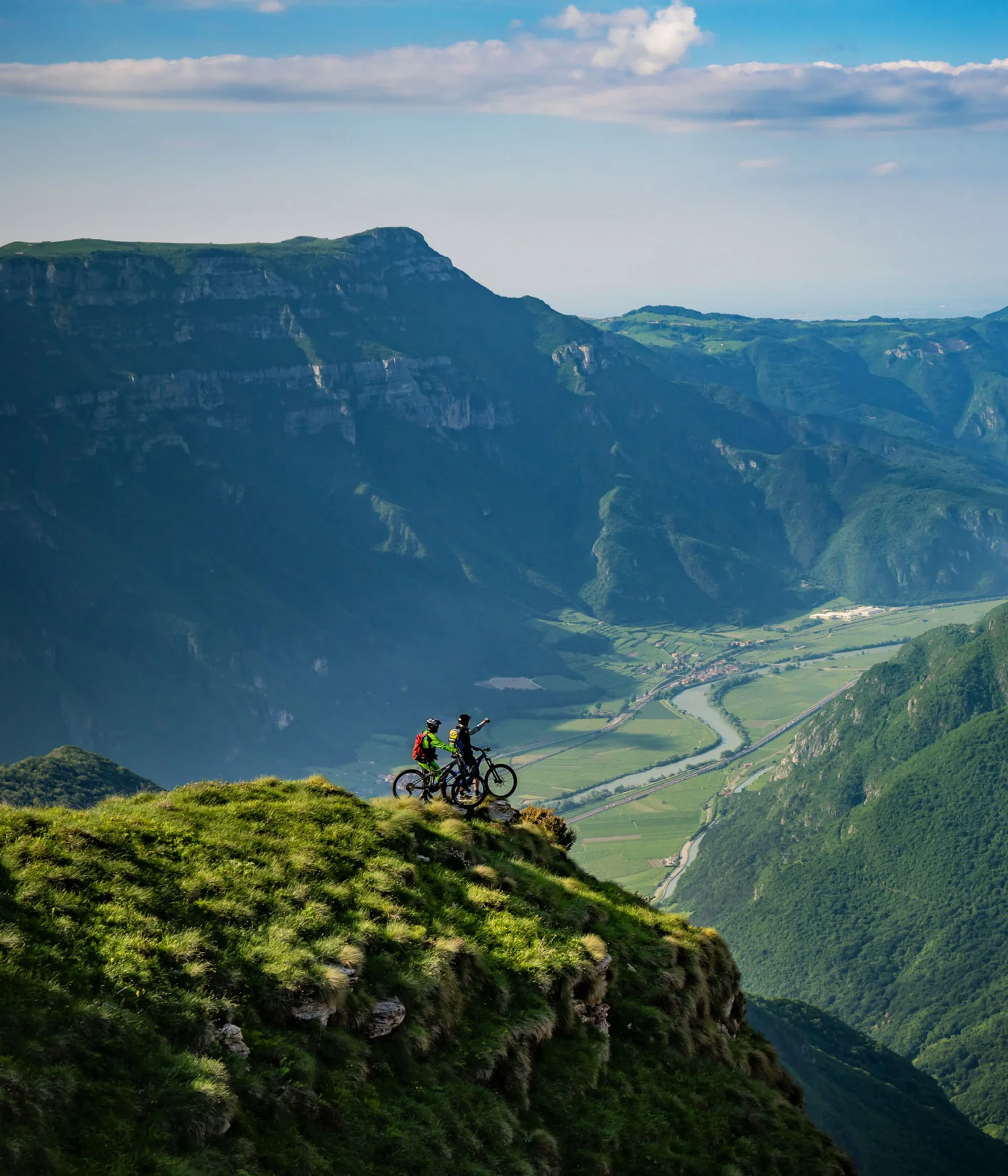 Elgus: hotel a 4 stelle in Trentino Due ciclisti su una cima erbosa con vista panoramica sulle montagne e la valle