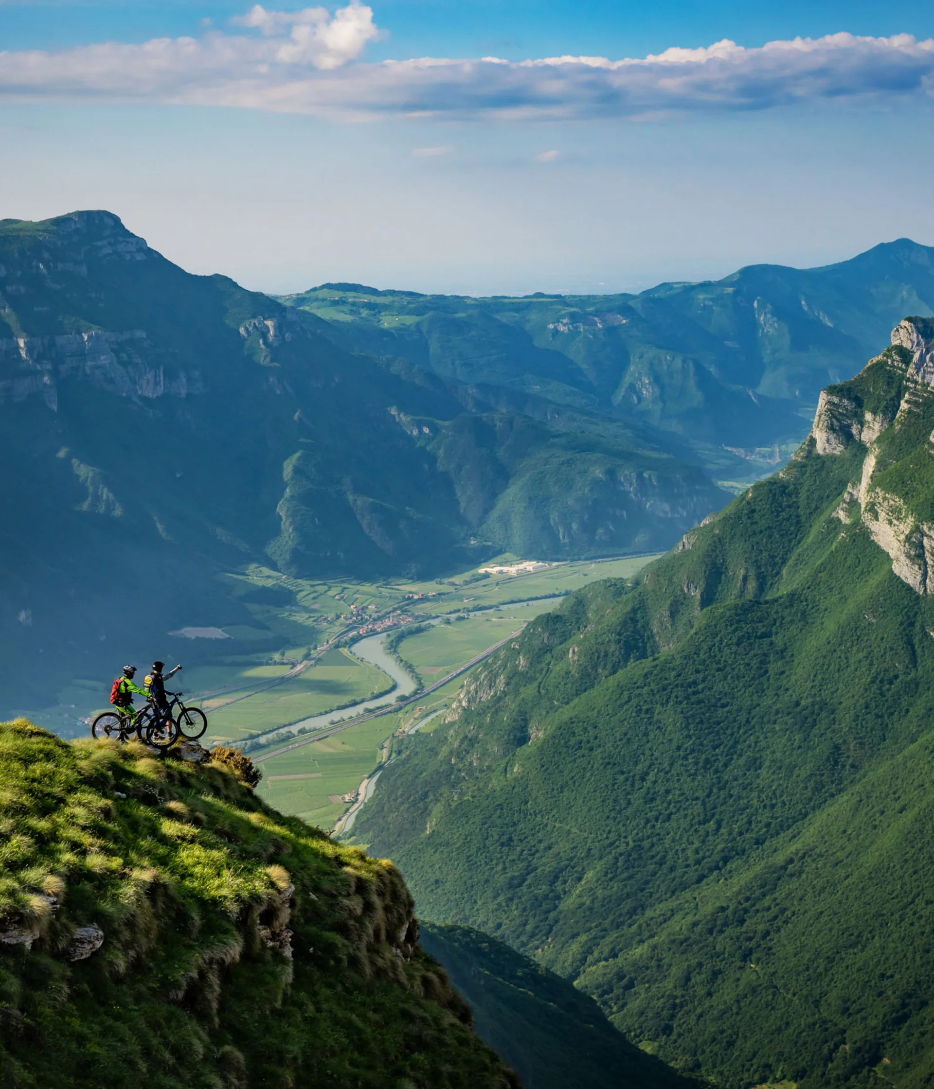Tutto il divertimento di un hotel sul Monte Baldo Due ciclisti su una cima erbosa con vista panoramica sulle montagne e la valle