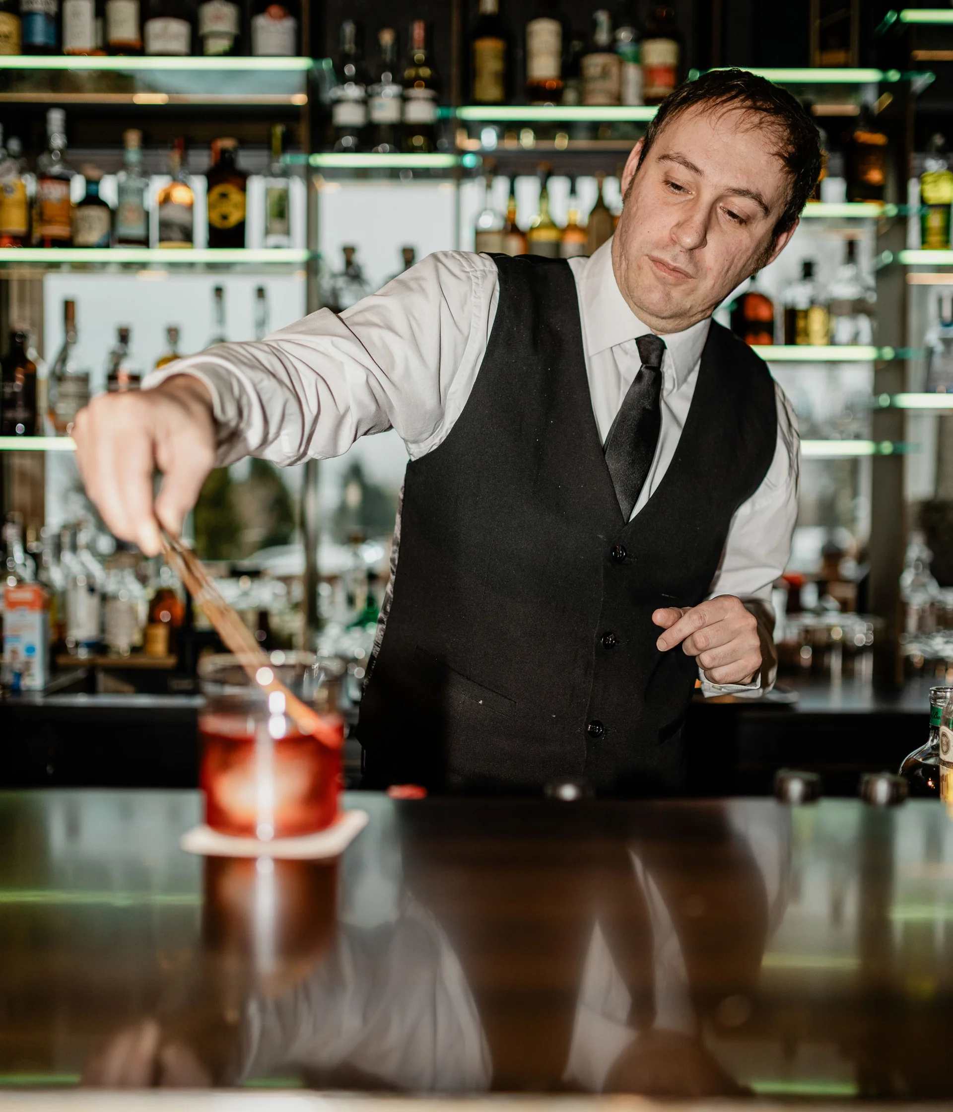 Elgus: hotel in Trentino con pensione ¾ Barista che prepara un cocktail al bancone con bottiglie sullo sfondo