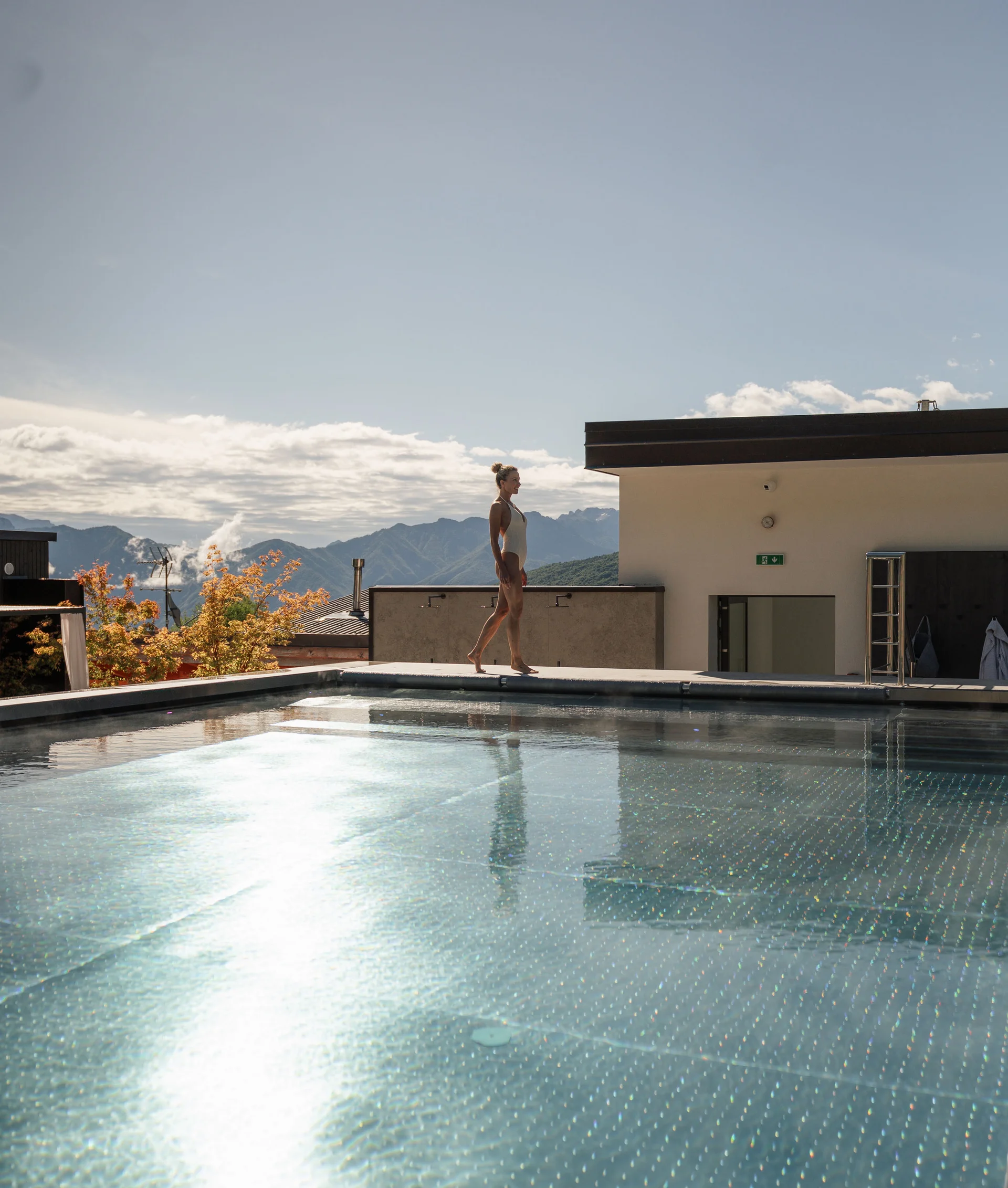 Elgus: hotel con spa adults only in Trentino Donna in costume da bagno cammina vicino a una piscina all'aperto con montagne sullo sfondo