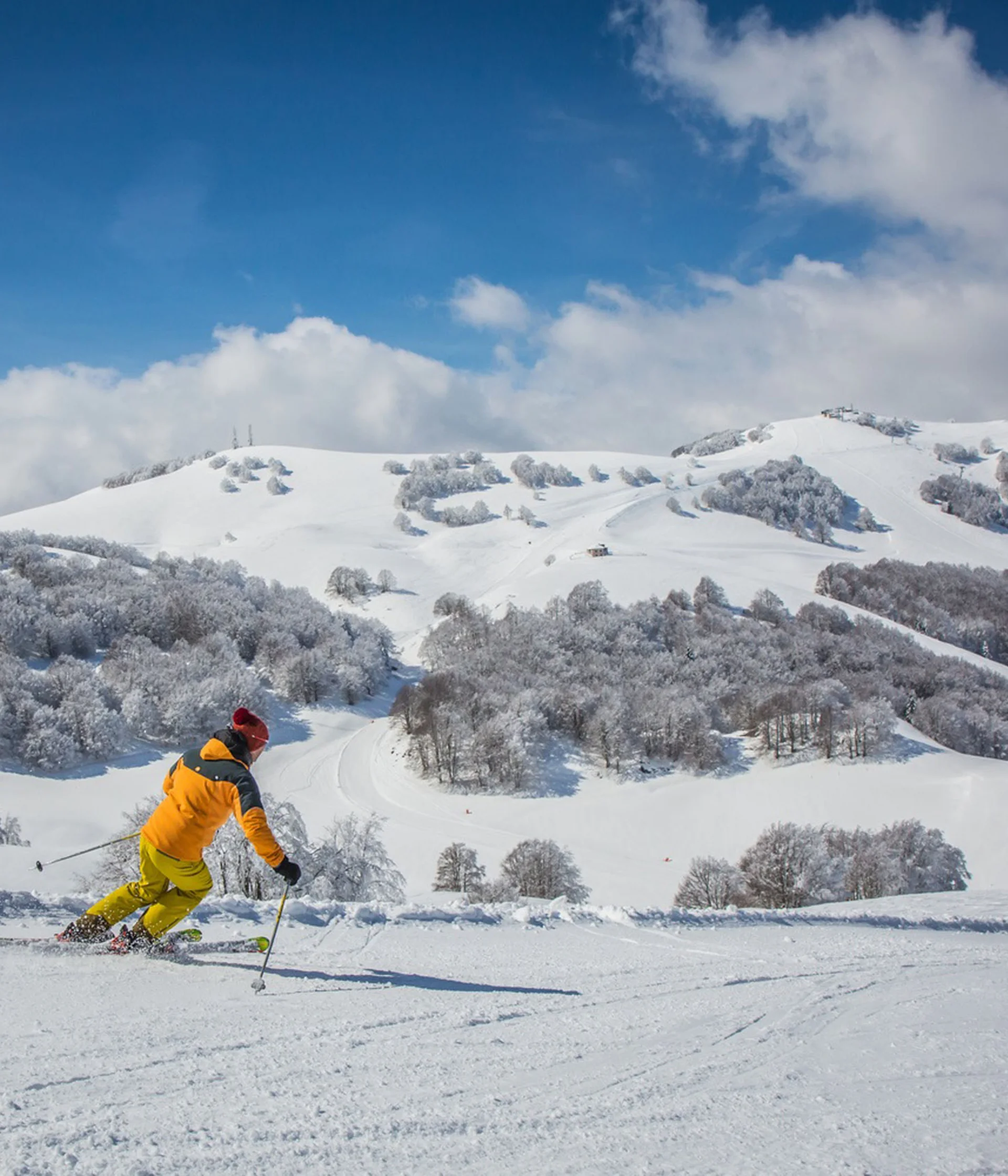 Tutto il divertimento di un hotel sul Monte Baldo Sciatore con giacca arancione e pantaloni gialli sulle piste innevate